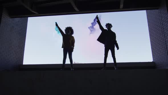 Mixed race man and woman holding blue and purple flares standing in an empty building