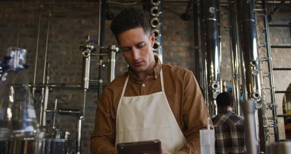 Caucasian man working at gin distillery, using digital tablet, wearing apron