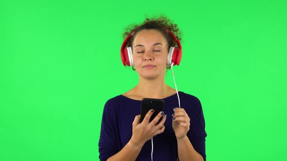 Portrait of Curly Woman Dancing and Enjoying Music in Big Red Headphones with Phone. Green Screen