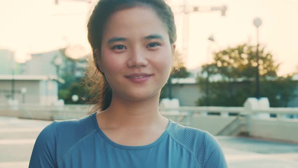 Portrait of smiling young Asian female while standing outside after workout in the park.