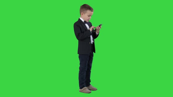 Young Boy in Elegance Suit Playing with Mobile Phone on a Green Screen, Chroma Key.