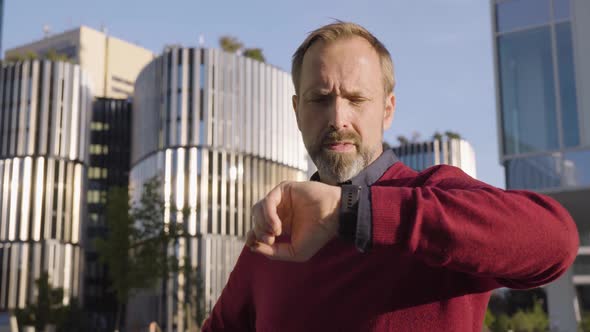 A Middleaged Handsome Caucasian Man Works on His Smartwatch in an Urban Area