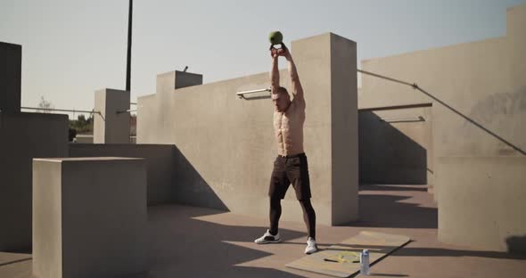 Sportsman Exercising with Kettlebell Outside Concrete Building