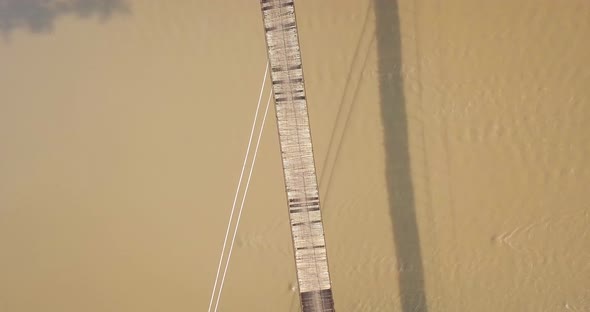 Top Down Drone Shot from a suspension bridge over a large river while a motorcyclist drives over it