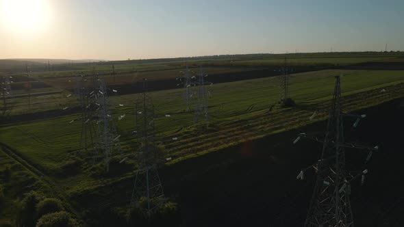 Drone Flying Over Transmission Tower Supporting an Overhead High Voltage Power Line at Sunset