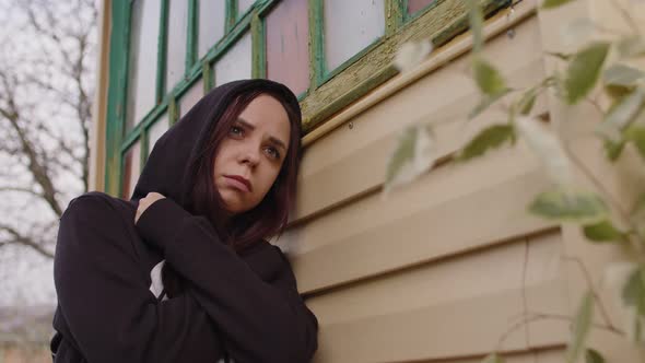 Close Up of Sad Woman with Arms Crossed Stands Leaning on House