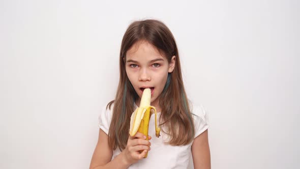 A Cute Teenage Girl Cleans and Eats a Banana Against a White Wall