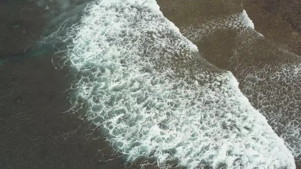 Aerial View of Breaking Waves Creating Seafoam Near the Shore.