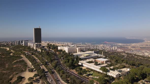 Flight to Haifa city around a tall building on a hill surrounded by trees and roads, with the harbor