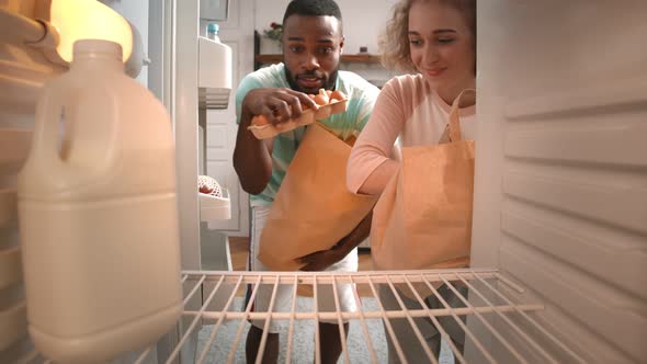 Multiethnic Young Couple Unpacking Groceries in Fridge