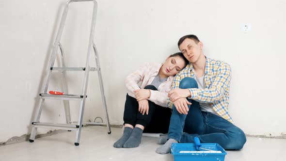 Tired Couple Sits at White New Apartment Wall Near Tray