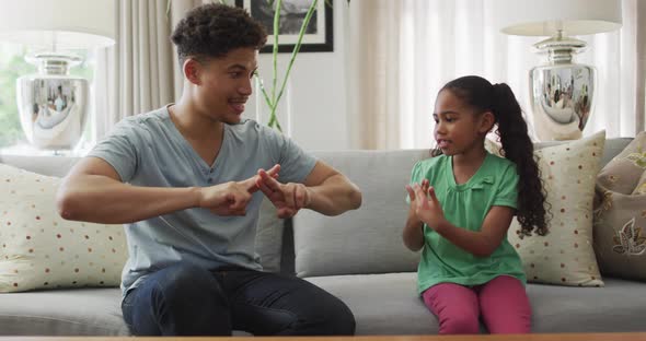 Happy biracial father and daughter sitting on sofa using sign language