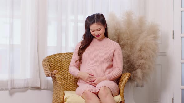 Happy Pregnant Woman sitting on couch holding and stroking her big belly at cozy home