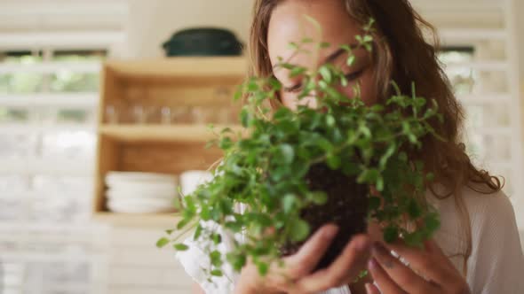 Happy caucasian woman smelling plant standing in cottage kitchen