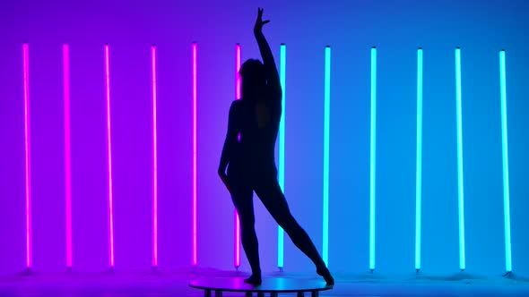 A Slim Athletic Woman in a Shiny Suit Moves Gracefully Against a Background of Pink and Blue Neon