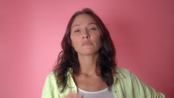 Woman Suspects Something Looks at the Camera Thoughtfully on a Pink Background