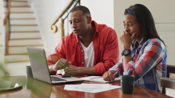 Stressed biracial couple sitting at table with laptop and counting home budget