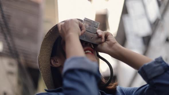 Beautiful female young Asian traveler wearing retro fedora hat using film camera taking a photo.