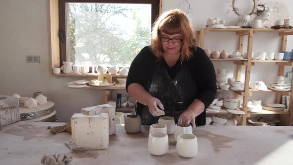 Woman with ceramic mugs in workshop near earthenware