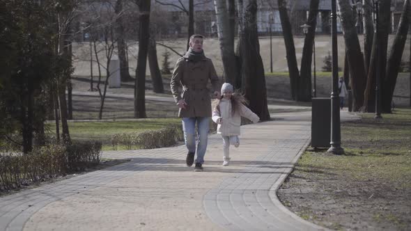 Cheerful Little Girl Running After Young Joyful Man Imitating Fear. Happy Father and Daughter Having