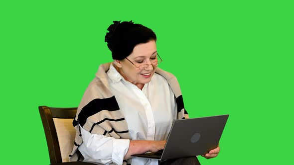 Senior Woman Sitting in Chair and Working on Laptop on a Green Screen Chroma Key