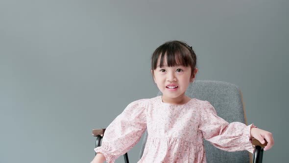 Child looking at camera and swing arms and pointing to something. Sitting in armchair in front of gr