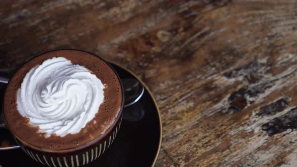 Hand Serving a Brown Mug of Plant Based Hot Chocolate with Whipped Cream on a Wooden Table