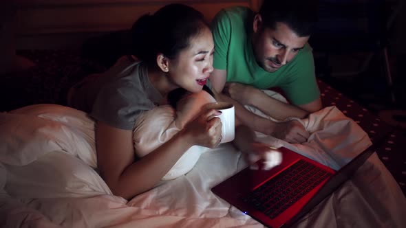 Happy multiethnic couple watching movie on laptop in bed