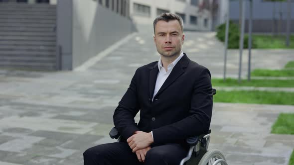 Portrait of Serious Man in Formal Suit Looking To Camera While Sitting at Wheel Chair