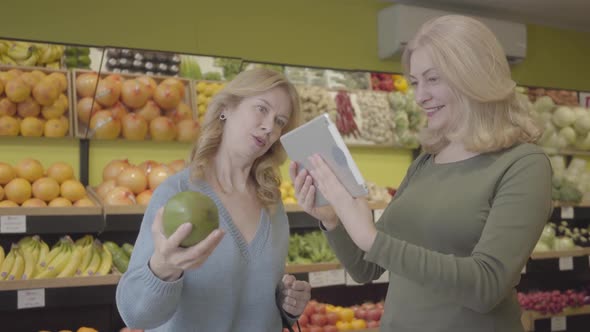 Adult Caucasian Women Checking Fruit Origin Using Tablet. Positive Housewives Buying Pomelo in