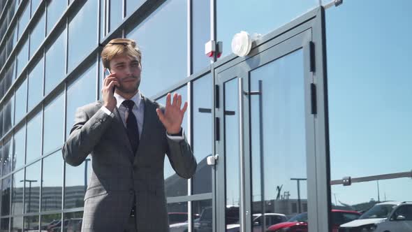 Young Businessman in a Suit Walking Near a Glass Skyscraper and Talking on a Mobile Phone, Top