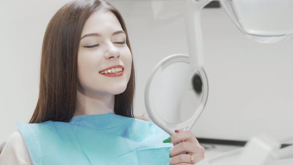 Beautiful Woman Examining Her Teeth in the Mirror at the Dental Clinic
