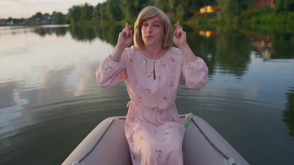 Positive Trans Woman Crossing Fingers Closing Eyes Making a Wish Sitting in Boat on Lake