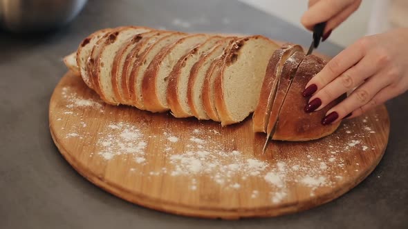 Woman Cuts Fresh Bread on a Wooden Board. Flour Around. Hands with Red Nails. Close Up.