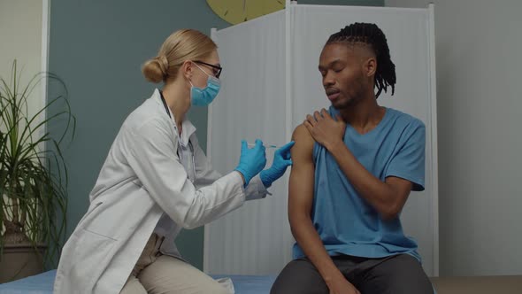 Young Man Taking Vaccination Shot Sitting on Diagnostic Bed Indoors