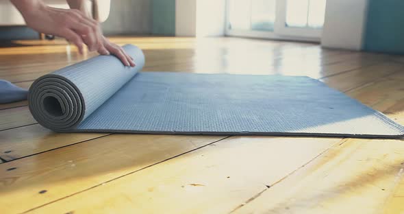 Lady Yoga Trainer Unrolls Grey Rubber Mat on Wooden Parquet