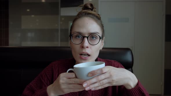 Cute Young Woman in Eyeglasses, Sitting in the Cafe and Talking To Someone