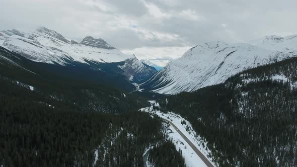 Drone shot of rocky snow-capped mountains covered with coniferous forest in Alberta, Canada