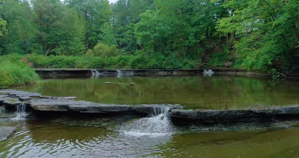 Drone footage of three small waterfalls that trickle into a pool of water.  Another larger waterfall