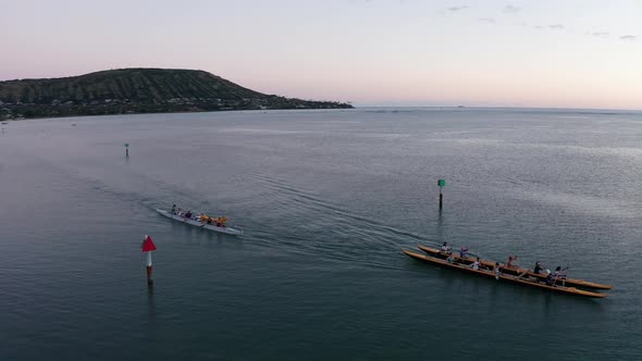 Aerial panning shot of a team of outrigger canoes paddling across the water in O'ahu, Hawaii. 4K