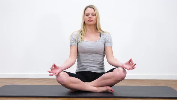 A Young Beautiful Woman Meditates in a Lotus Position in a Room