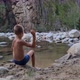 a boy plays on the riverbank, throws stones into the water - VideoHive Item for Sale