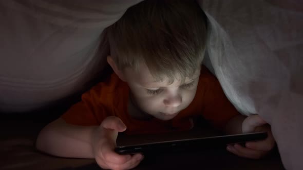 Small boy looking a tablet in bed under the covers