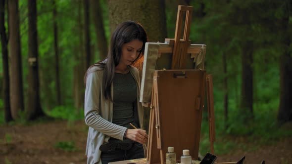 Side View of a Young Woman Painting a Landscape in a Park.