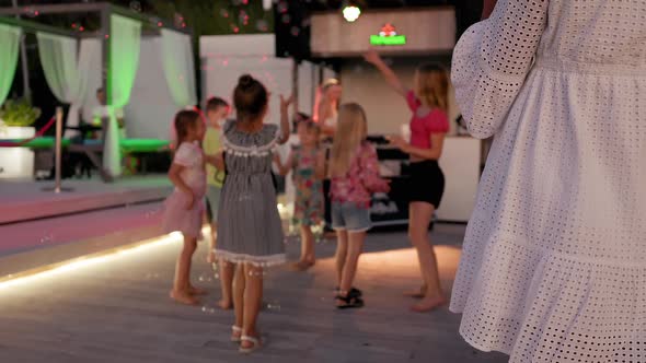 Blurry Kids Play with Bubbles at a Beach Bar Party at Night