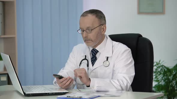 Doctor Reading Medical Reference Book in Special Application on His Smartphone