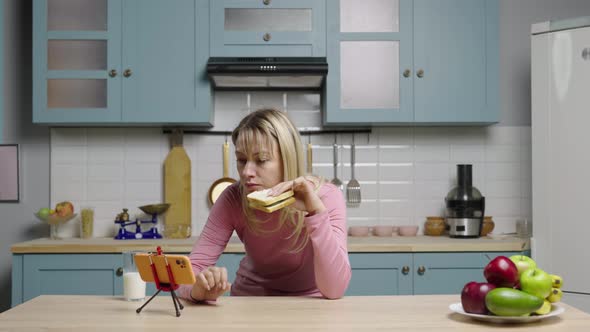 Young Woman Watching Funny Videos on Social Media Using Phone Eating Sandwich and Laughing