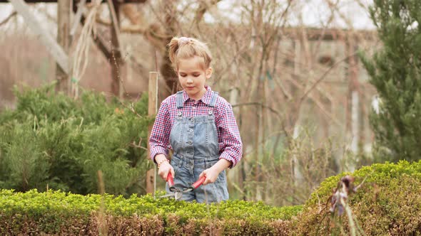 a Funny Little Girl Cuts Bushes in the Garden with Large Pruner