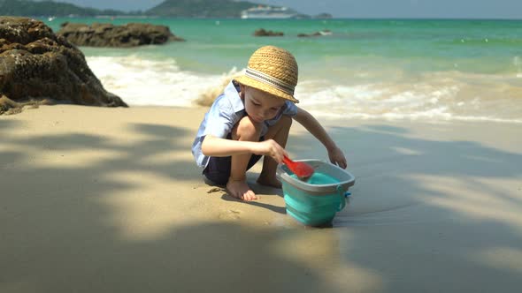 Boy Playing on the Beach By the Sea. He Digs Sand and Throws It in the Bucket