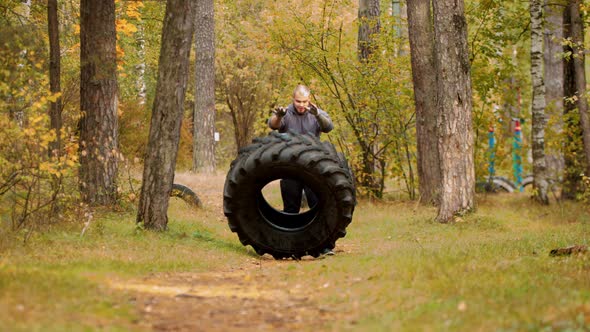 A Big Man Bodybuilder Turning Over the Tire on the Ground and Moving It Forward - Training Outdoors